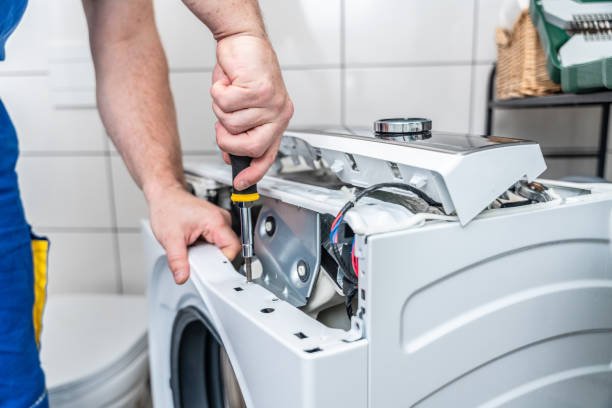 Technician opening the top panel of a washing machine with a screwdriver